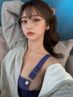 Woman with long hair and round glasses wearing a hoodie and blue top indoors