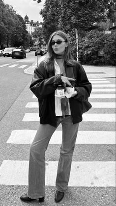 Woman in sunglasses and a leather jacket holding coffee on a street crossing