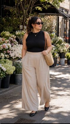 Woman in a black top and wide leg pants standing outside a flower shop