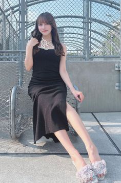 Woman in a black dress and ruffle sandals sitting outdoors by a fence