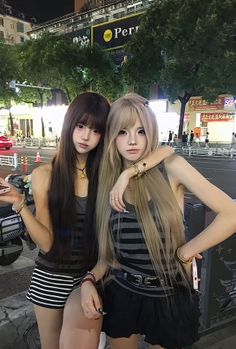 Two women with long hair posing on a city street at night