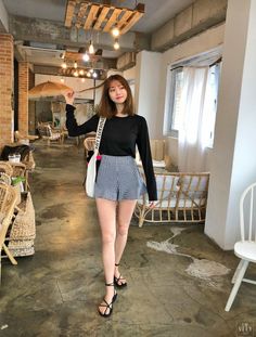 Woman in a black top and gingham shorts walking in a cafe