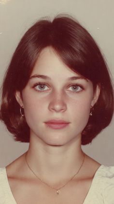 Young woman with short brown hair and blue eyes wearing earrings and a necklace