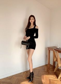 Woman in a black mini dress and high heels holding a small bag indoors