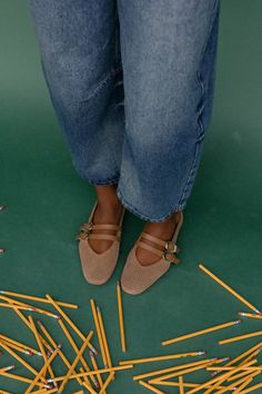 Person in blue jeans and mary jane shoes standing on a green surface with scattered pencils