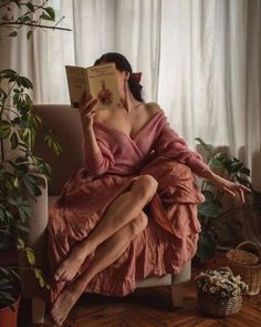 Woman in a pink dress reading a book indoors with plants