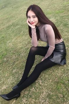 Woman with long hair wearing a leather skirt and black tights sitting on grass