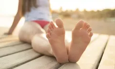 Person in a red bikini bottom with bare feet on wooden planks at golden hour