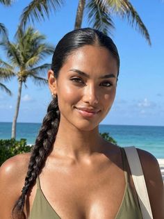 Woman with braided hair smiling at the beach with palm trees and blue sky