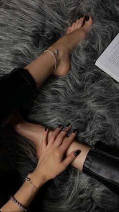 Person with black nail polish and jewelry on a fur rug