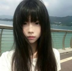 Young person with long black hair and bangs outdoors by a waterfront
