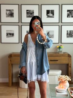 Woman in a white dress and denim shirt taking a mirror selfie indoors