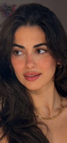 Woman with long dark hair and gold jewelry looking to the side