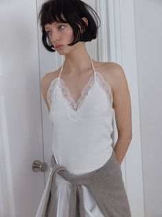 Woman with short dark hair wearing a white lace-trim halter top indoors