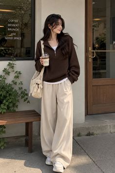 Woman in a brown sweater and wide leg pants holding a coffee outside a cafe