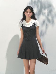 Woman in a dark pleated dress over a white shirt, holding a brown bag