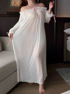 Woman in a sheer white nightgown with pink ribbons standing indoors