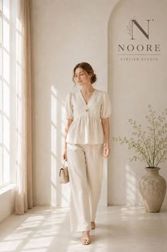 Woman in a neutral linen top and pants holding a small handbag indoors