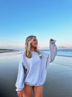 Woman with long blonde hair in an oversized sweatshirt on a beach at sunset