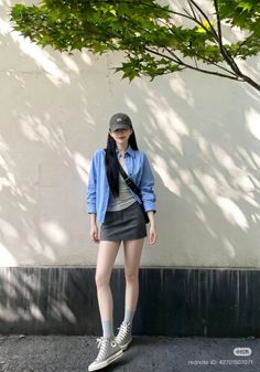 Woman in a blue shirt and mini skirt standing outdoors with tree shadows on a wall