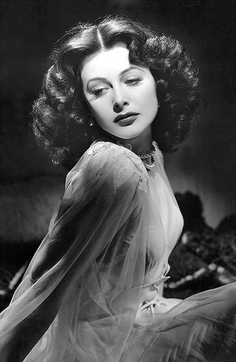 Woman with curly hair and a pearl necklace in a soft-lit black and white portrait