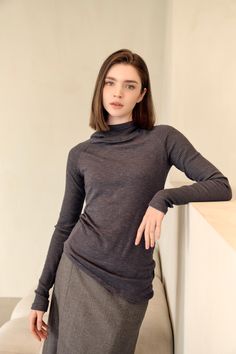 Woman with short brown hair wearing a grey turtleneck and skirt indoors