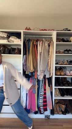 Person in a cardigan and jeans in front of a closet with clothes and shoes