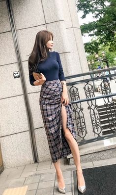 Woman in a plaid skirt and long-sleeved top standing outdoors