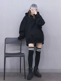 Person in an oversized black hoodie, thigh-high socks, and a baseball cap taking a selfie