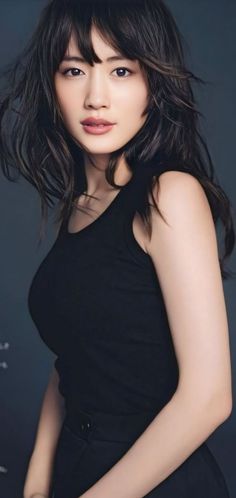 Woman with long black hair wearing a black tank top against a dark background