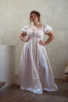 Woman in a long light-colored dress with puffy sleeves standing indoors