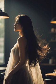 Woman with long hair in a sheer dress, lit by soft backlight indoors