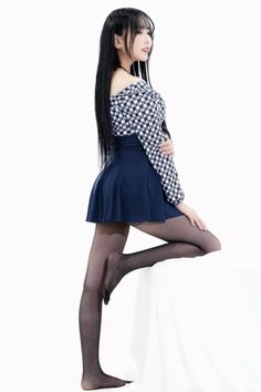 Woman with long black hair in an off-shoulder top and mini skirt posing in a studio