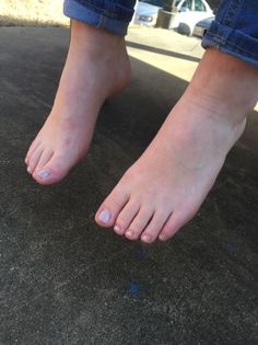 Bare feet with light nail polish and rolled-up jeans on concrete ground