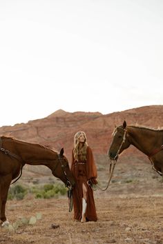 Woman in a brown dress and cowboy boots with two horses in a desert landscape