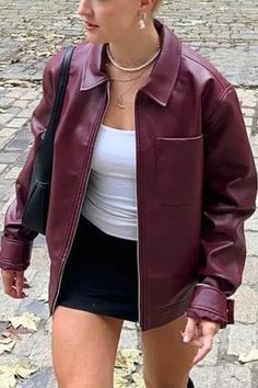 Woman in a burgundy leather jacket, white tank top, and black mini skirt outdoors