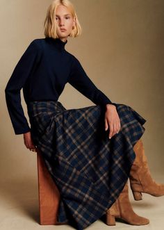 Woman with blonde hair wearing a turtleneck, plaid skirt, and brown boots