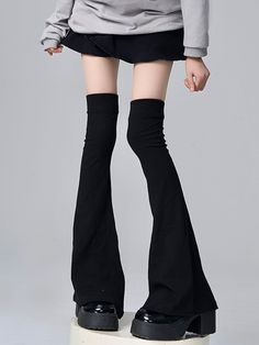 Person in a black skirt, gray hoodie, and black leg warmers with platform shoes