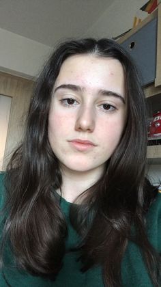 Young woman with long dark hair wearing a green top indoors