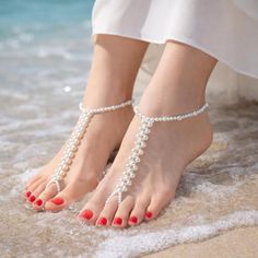 Feet with pearl barefoot sandals and red nail polish on a sandy beach