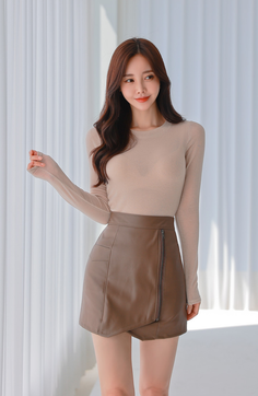 Woman with long brown hair wearing a sheer top and brown leather skirt indoors