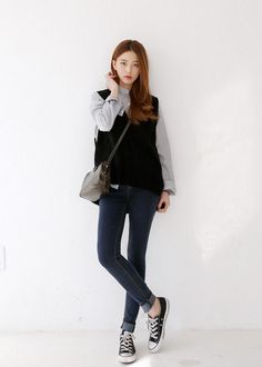 Woman in a striped shirt, black vest, and skinny jeans posing indoors