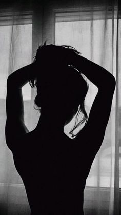 Silhouette of a person with hands behind their head, backlit by a window
