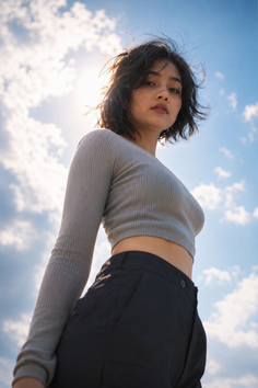 Woman with short hair in a crop top and black pants against a blue sky