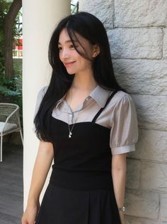 Woman with long black hair wearing a collared shirt and black top outdoors