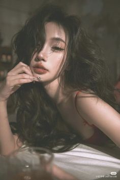 Woman with long dark hair in red lingerie, posing indoors with soft lighting