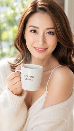 Woman in a white sweater holding a coffee mug, smiling at the camera