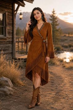 Woman in a brown suede fringe dress and cowboy boots outdoors at golden hour