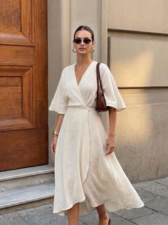 Woman in a cream wrap dress and sunglasses standing outdoors
