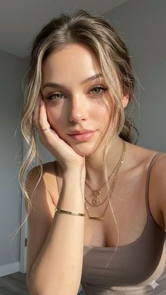Woman with blonde hair and green eyes wearing gold jewelry and a tank top